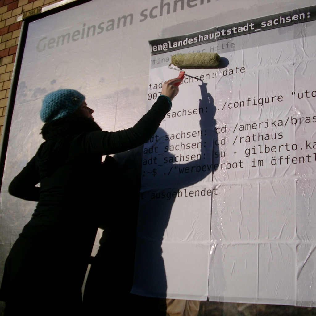 Die Künstlerin beim Überkleben einer kommerziellen Plakatwand: Die neue Schicht Plakate sieht aus wie eine Shell, in der die Kommandos ein Werbeverbot im öffentlichen Raum fordern.