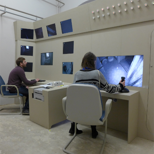 2 junge Menschen arbeiten in einem Kontrollraum mit 9 Monitoren.