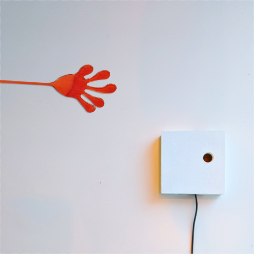 Eine Spielzeughand aus glibberigem, orangefarbenem Silikon haftet quer an einer Wand.