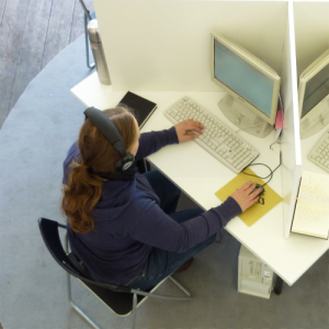Eine Frau mit langen brünetten Haaren und einem Headset steuert mit Tastatur und Maus ein Voice-Over-IP-Programm.