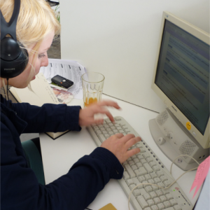 Eine blonde, junge Frau mit Headset füllt mit fliegenden Fingern ein Formular am Computer aus.