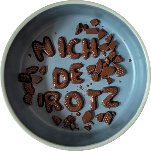In einer Schale aus hellblauem Steingut schmelzen Schokoladen-Buchstaben und Bruchstücke davon. Lesbar ist nur noch: NICH DE ROTZ
